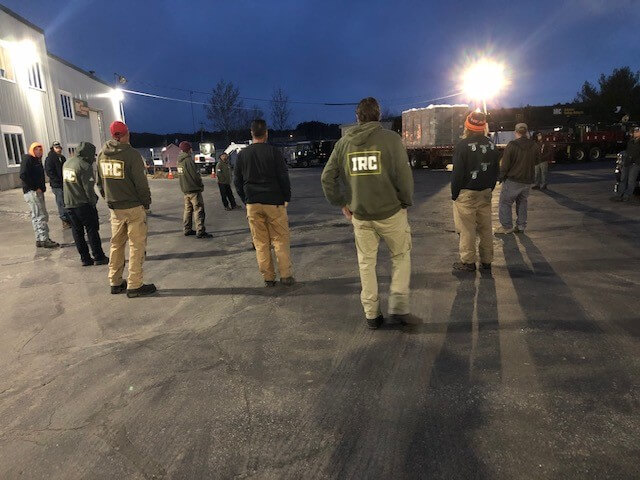 Industrial roofing contractor employees standing socially distanced in a parking lot for a meeting