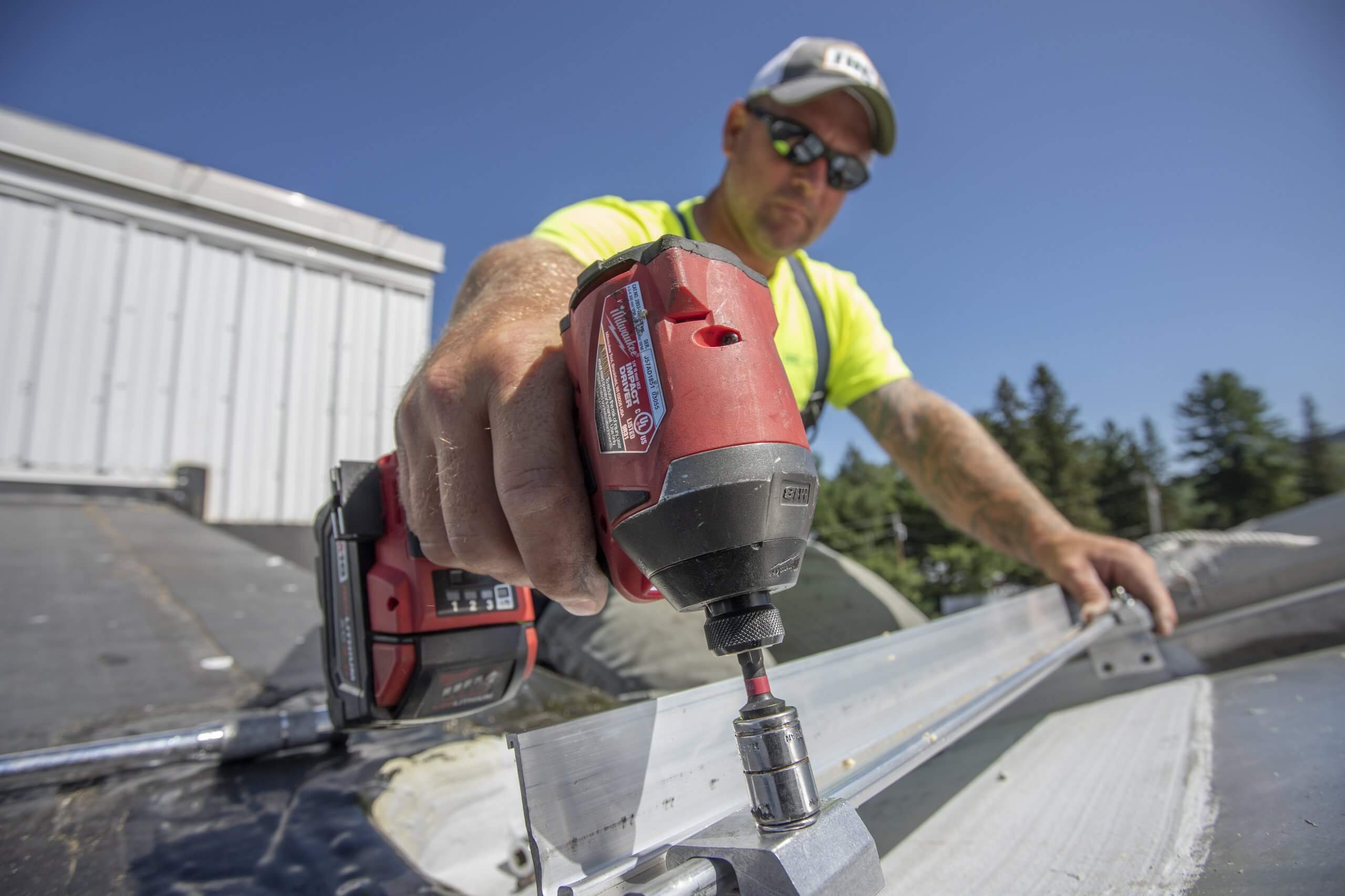 A roofing technician uses a drill to install a new part to a roof