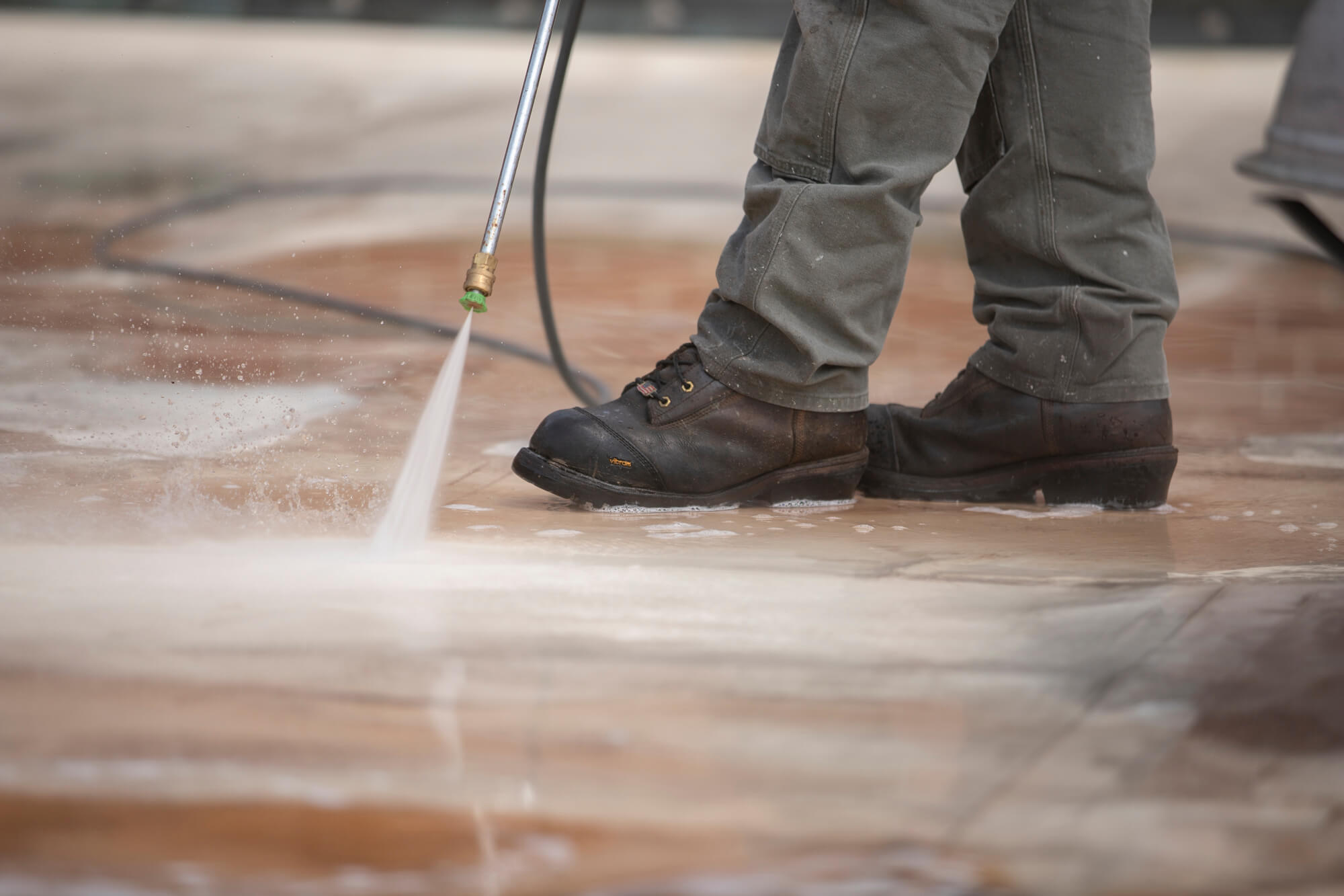 A roofing technician power washes a roof, only his legs and power washer are visible